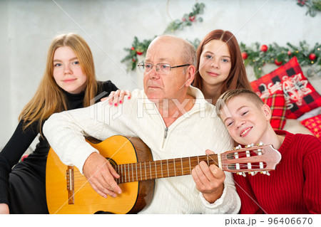 Grandfather playing guitar during christmas for grandchildren. Happy man 60s playing guitar christmas songs. Grandfather playing guitar during christmas for grandchildren. Happy man 60s playing guitar christmas songs. 96406670