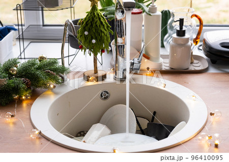 Dirty dishes in the sink in the garlanded kitchen, a holiday after a feast at Christmas. Mess after the guests for the New Year, kitchen cleaning, detergent, cleaning services Dirty dishes in the sink in the garlanded kitchen, a holiday after a feast at Christmas. Mess after the guests for the New Year, kitchen cleaning, detergent, cleaning services 96410095