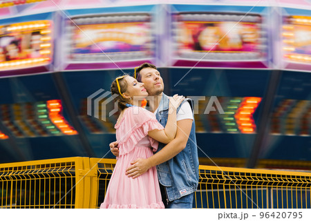 Happy couple in love enjoying each other in an amusement park and cuddling Happy couple in love enjoying each other in an amusement park and cuddling 96420795