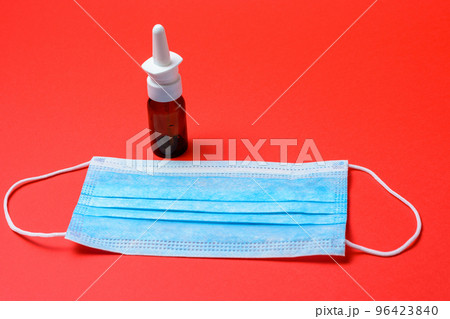On a red background, a bottle for runny nose and allergy, medical mask. 96423840
