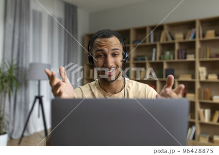 Happy arab man in headphones having video call on laptop, talking and gesturing at computer webcamera in home office 96428875