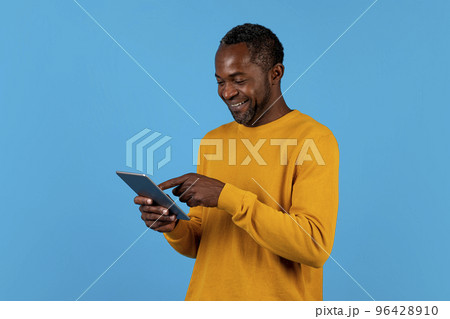 Cheerful black man using digital tablet isolated on blue Cheerful black man using digital tablet isolated on blue 96428910