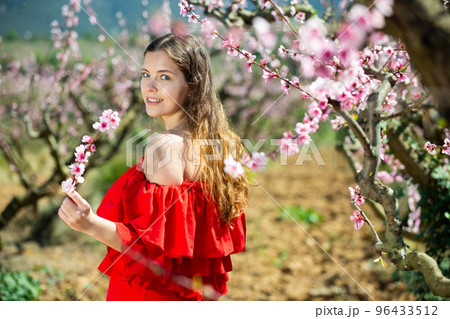 Woman in red dress standing near blooming peach tree 96433512