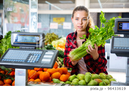Portrait of young positive woman customer buying fresh celery 96433619