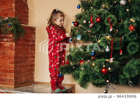 Adorable little girl decorating a Christmas tree with colorful glass baubles at home 96439906