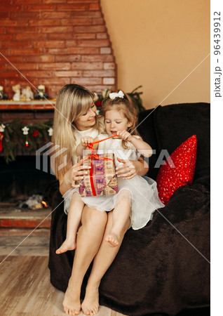 A happy mother and a girl with a gift box on the background of the fireplace. Christmas, holidays, celebrations, gifts 96439912