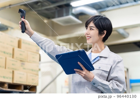 倉庫で電子機器を持って作業する女性従業員 96440130