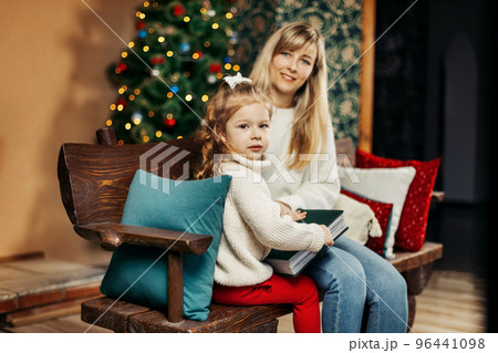 Cute mom and daughter are looking through a family photo album on Christmas Eve, spending time together by the fireplace and the Christmas tree. Christmas, New Year, memories, family evening Cute mom and daughter are looking through a family photo album on Christmas Eve, spending time together by the fireplace and the Christmas tree. Christmas, New Year, memories, family evening 96441098