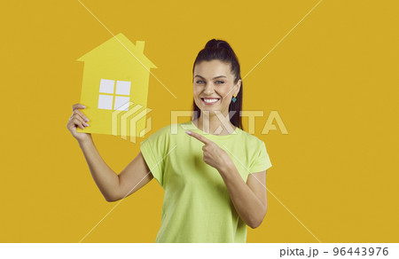 Studio portrait of happy young woman smiling and pointing at paper house in her hand 96443976