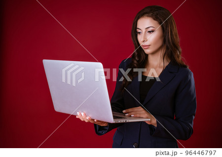 Young woman decides business cases in a laptop on a red studio background. Young woman decides business cases in a laptop on a red studio background. 96446797