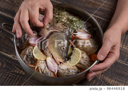 The hands of the cook put the head of a carp in a pan with fish meatballs 96446918