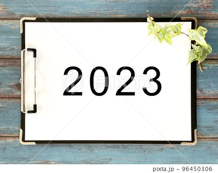 クリップボードに挟んだ2023文字入り白い用紙_青色木板背景 96450306