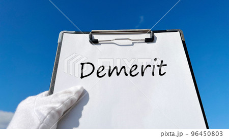 Demeritの文字入りクリップボードを持つ白手袋の手_青空背景 96450803