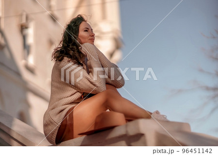 Woman walks in the city, lifestyle. Young beautiful woman in a loose light sweater, brown skirt and sneakers with a hat. 96451142