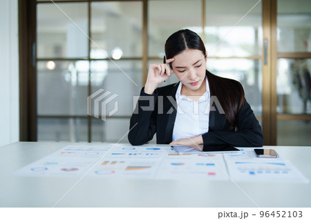 A portrait of a beautiful Asian female employee showing a stressed face while using financial documents on her desk. A portrait of a beautiful Asian female employee showing a stressed face while using financial documents on her desk. 96452103