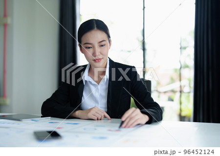 Portrait of a thoughtful Asian businesswoman looking at financial statements and making marketing plans using a tablet computer on her desk. 96452124
