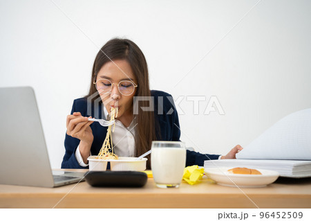 Busy and tired businesswoman eating spaghetti for lunch at the Desk office and working to deliver financial statements to a boss. Overworked and unhealthy for ready meals, burnout concept. 96452509