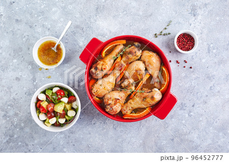Chicken drumsticks with oranges and thyme baked in red round baking dish 96452777