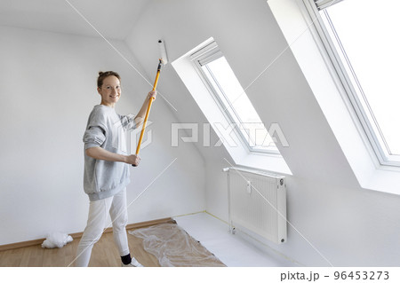 Portrait young adult beautiful single happy woman painting wall paint roller brush white color living room moving new home flat . Female painter decorating interior renovation residential apartment 96453273