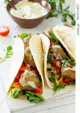 Arabic cuisine. Concept of vegetarian food. Delicious fresh homemade vegetarian tortilla with falafel close-up on a wooden kitchen table. Street food, fast food. Arabic cuisine. Concept of vegetarian food. Delicious fresh homemade vegetarian tortilla with falafel close-up on a wooden kitchen table. Street food, fast food. 96455907