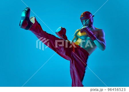 Workout of professional athlete. Kickboxer in helmet and gloves training isolated over blue background in neon light. Muay thai. Sport, competition, energy, combat sports 96456523