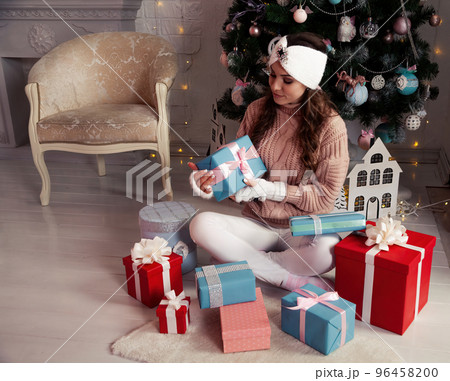 Happy woman with presents in front of the Christmas tree. Stylish female in cozy knitted sweater Happy woman with presents in front of the Christmas tree. Stylish female in cozy knitted sweater 96458200
