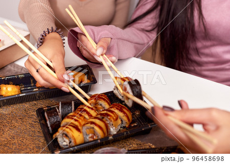 Portrait of three beautiful young women eating japanese food and drinking wine at home. Portrait of three beautiful young women eating japanese food and drinking wine at home. 96458698