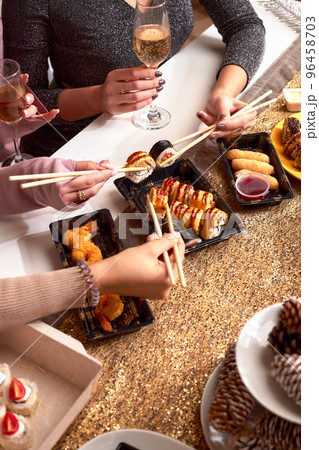 Portrait of three beautiful young women eating japanese food and drinking wine at home. Portrait of three beautiful young women eating japanese food and drinking wine at home. 96458703