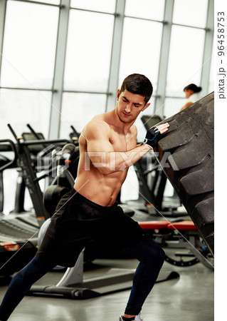 Muscular fitness man moving large tire in gym center, concept lifting, workout training. Muscular fitness man moving large tire in gym center, concept lifting, workout training. 96458753