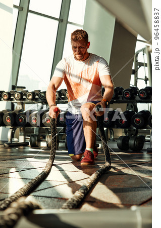 Athletic young man with battle rope doing exercise in functional training fitness gym 96458837