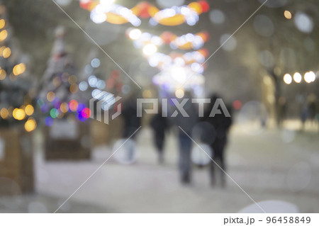 Abstract blurred background. People walking on street of decorated Christmas trees decorated with luminous illumination, glowing lights and garlands in city during heavy snowfall on winter night 96458849