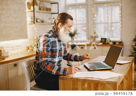 Old man with laptop. Grandfather sitting in a Christmas decorations. Man in a cell shirt. 96459178