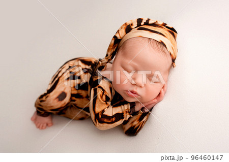 Sleeping newborn girl in the first days of life on a white background. Macro studio portrait of a child. Image of a tiger cub. Newborn baby in tiger pajamas. Striped black and orange baby clothes. 96460147