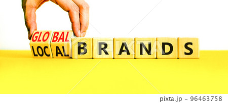 Global or local brands symbol. Concept words Global brands and Local brands on wooden cubes. Businessman hand. Beautiful yellow table white background. Business global local brand concept. Copy space. Global or local brands symbol. Concept words Global brands and Local brands on wooden cubes. Businessman hand. Beautiful yellow table white background. Business global local brand concept. Copy space. 96463758