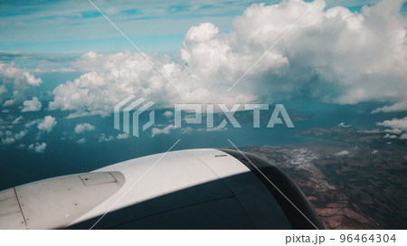 View from Boeing 737 MAX 8 on White Air Clouds, Clear Blue Sky And Surface Of Earth With Fields And Mountains. In frame White-Grey Engine Casing With Vanes. View from Boeing 737 MAX 8 on White Air Clouds, Clear Blue Sky And Surface Of Earth With Fields And Mountains. In frame White-Grey Engine Casing With Vanes. 96464304