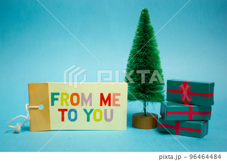 A gift under the toy Christmas tree on Happy New Year 2023. Merry Christmas presents in green boxes. Winter vacations, holidays celebration. A note from Santa Claus with the text From me to you. 96464484