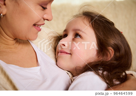 Close-up of a cute child, adorable lovely baby girl smiling cutely looking at her loving mother hugging her. Happy carefree childhood. Love Affection Tenderness. Mother's and Children's Day concept 96464599