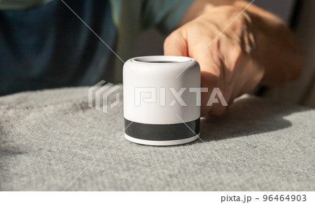 Man hand closeup removing lint from fabric with shaver. Handheld electric device for cleaning clothes from fluff, dust Man hand closeup removing lint from fabric with shaver. Handheld electric device for cleaning clothes from fluff, dust 96464903