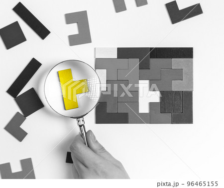Hand with magnifier over suitable outstanding puzzle piece. Logical thinking, situation analysis concept. Important missing element adding. Uniqueness, individuality concept 96465155