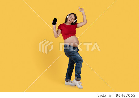 Cheerful Pregnant Woman Wearing Wireless Headphones Listening Music On Smartphone And Dancing Cheerful Pregnant Woman Wearing Wireless Headphones Listening Music On Smartphone And Dancing 96467055