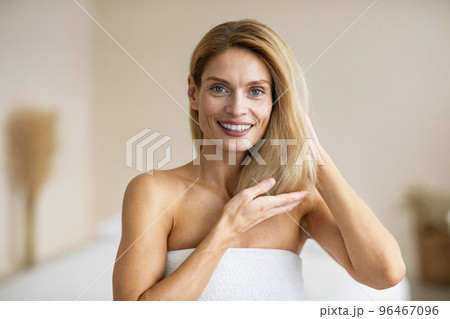 Portrait of happy middle aged woman touching her soft hair, standing in bedroom and smiling at camera 96467096