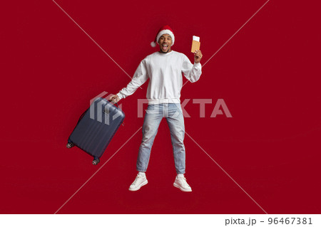 Black guy tourist in Santa hat jumping over red background Black guy tourist in Santa hat jumping over red background 96467381