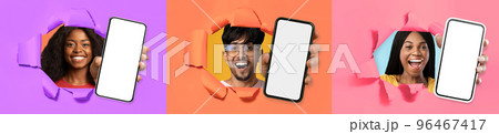 Three cheerful youngsters showing smartphones through hole in paper wall Three cheerful youngsters showing smartphones through hole in paper wall 96467417