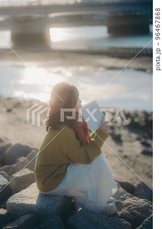 河川敷で本を読みながら佇む若い女性の写真 河川敷で本を読みながら佇む若い女性の写真 96467868