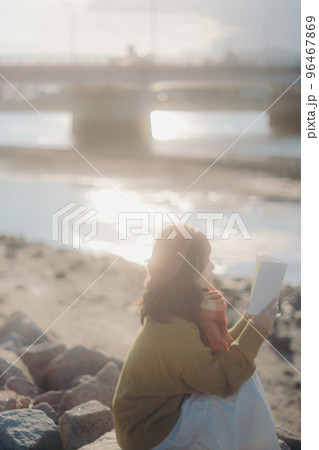 河川敷で本を読みながら佇む若い女性の写真 96467869