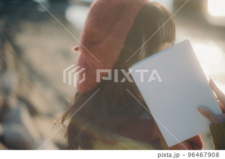 河川敷で本を読みながら佇む若い女性の写真 96467908