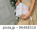 Closeup shot of female hands holding beautiful Christmas present with pink ribbon on white background in interior 96468310