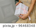 Closeup shot of female hands holding beautiful Christmas present with pink ribbon on white background in interior 96468348