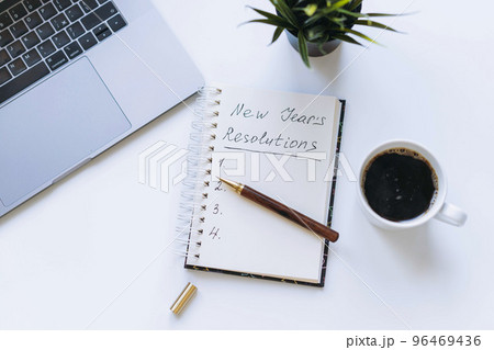 open notepad with new year resolutions and empty list. Flower, laptop and coffee cup on background. open notepad with new year resolutions and empty list. Flower, laptop and coffee cup on background. 96469436