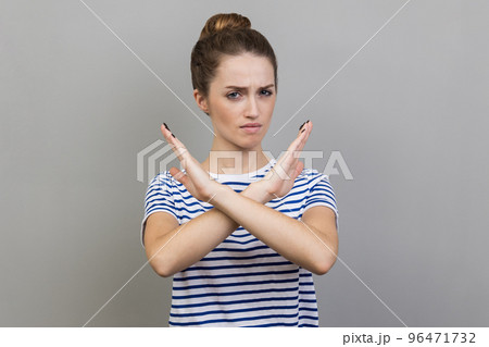 No way, absolutely not. Portrait of woman wearing striped T-shirt showing x sign with crossed hands, meaning stop, this is the end. Indoor studio shot isolated on gray background. 96471732